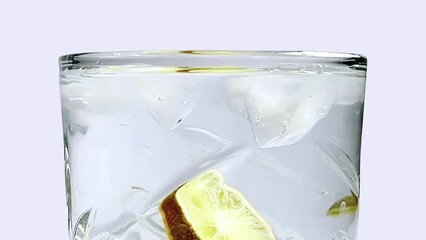 slow motion shot of lemon water with ice in a glass, detox water in a glass with ice cubes, lemonade in a glass