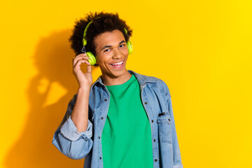 Photo of nice young man touch headphones empty space wear denim shirt isolated on yellow color...