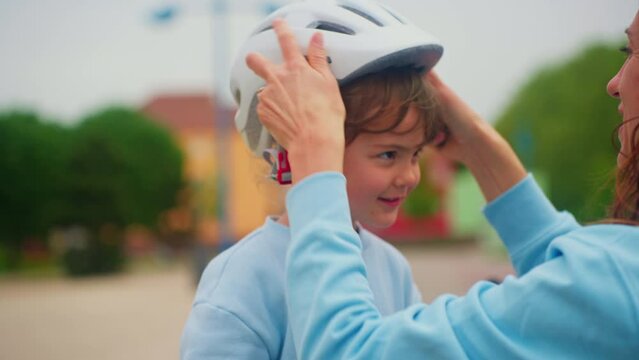 Loving mother put on sport helmet to little cute kid daughter before spin bicycle on street. Little girl wear protective halmet for health care and safety