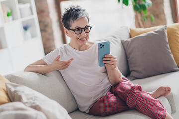 Photo of pretty retired woman hold device video call sofa wear white outfit home flat rest relax...
