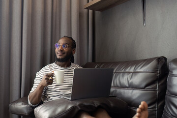 young attractive african working at home and use laptop checking schedule working process and relax on sofa in living room with morning light peaceful moment
