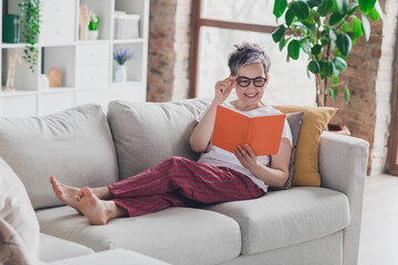 Full length photo of lovely mature lady sit sofa read book dressed white garment modern living room...