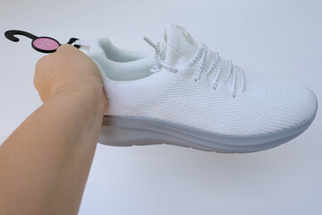 female hands holding new white trekking shoes, tied with laces on light background, concept Shoe...