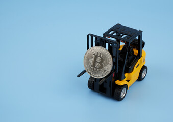 Forklift truck carrying bitcoin coin on blue background, copy space for text.