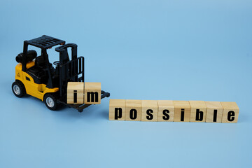 Forklift truck takes out letters im from word impossible on blue background.