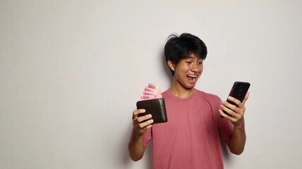 young asian man happily holding and looking at money wallet and smartphone