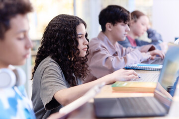 Portrait of multiethnic young girl using laptop in school with students sitting in row copy space