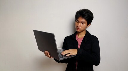 young asian student is standing holding a laptop