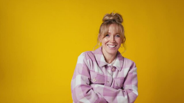 Portrait of casually dressed laughing woman with folded arms standing against yellow studio background - shot in slow motion