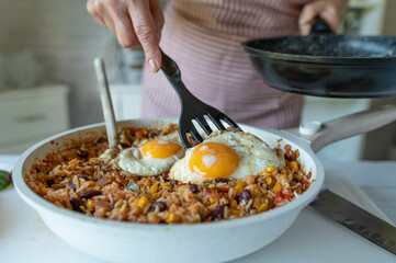 Woman serving fresh fried egg, sunny side up on a healthy rice dish in the kitchen