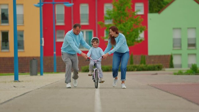 Happy parents educate child ride bicycle with encourage and support. They let go the girl successfully and happily clap
