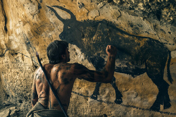 Homo sapiens en train de dessiner la peinture rupestre  d'un bovin dans une grotte avec un morceau de charbon