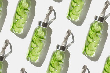 Cucumber water drink detox in glass bottles at sunlight as trend pattern on white. Wellness, diet,...