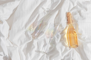 Rainbow color shining champagne glasses and white sparkling wine bottle on bed, on white blanket...