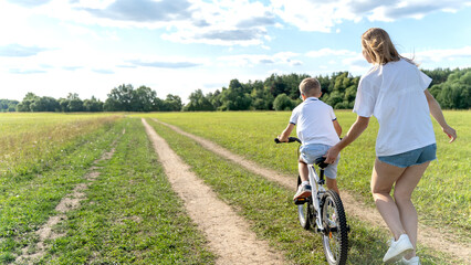 Fototapeta premium Mom teaches her son to ride a bike in nature