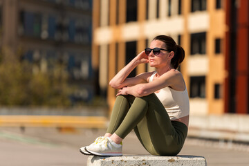 Sporty woman sitting resting in the sun after exercise outside, urban background