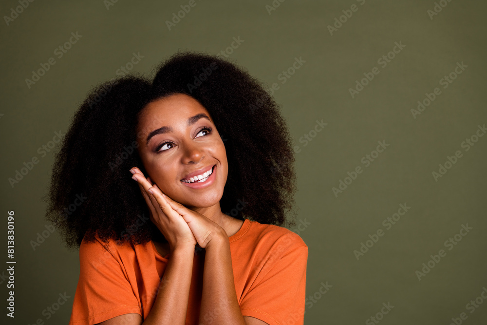 Wall mural Portrait of optimistic girl with wavy hairstyle wear orange t-shirt dreamy look at offer empty space isolated on dark khaki background