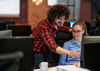 Business colleagues, a man and a woman, engage in discussing business strategies while attentively gazing at a computer monitor, epitomizing collaboration and innovation