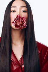 Attractive woman with long black hair wearing a red jacket and holding a flower in her mouth