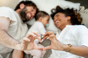 Happy family lying in bedroom making heart shape with hands - Married couple taking care of little...