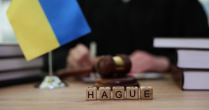 Word hague on cubes and flag of ukraine and judges in courtroom. UN Court in hague ordered Russia to stop hostilities and war on territory of Ukraine