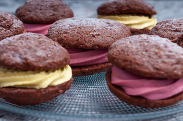 Brown cookies sandwiches with yellow and pink cream on transparent plate