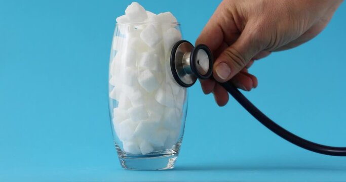 Doctor hand holds stethoscope on glass full of white sugar. Sweet food ingredient health and high risk of diabetes and calorie intake
