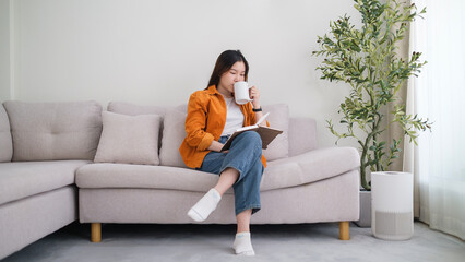 Beautiful young woman reading book on cozy sofa, spending leisure weekend tine at home.