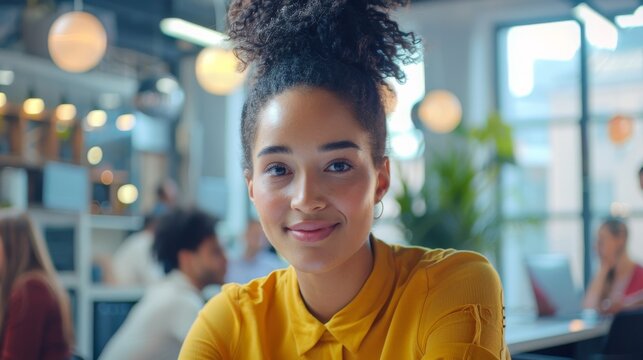 A young woman working on her computer in a bright busy office with a smiling female manager. People working in the background are also seen working on the computer.