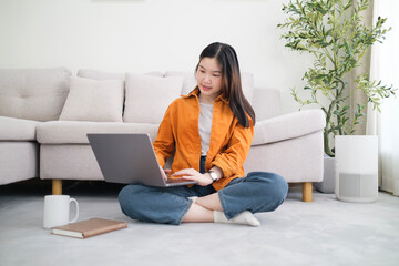 Beautiful young woman working with laptop while sitting on carpet in living room.