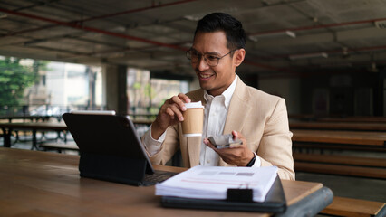 Smiling millennial businessman using digital tablet and working with financial reports.