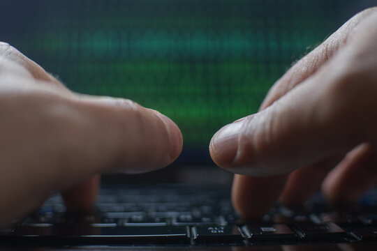 Male hands typing on a laptop keyboard with a green binary code in the background