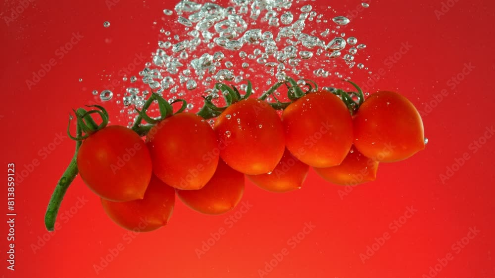 Poster super slow motion of falling cherry tomatoes. splashing into water on colored background. filmed on 