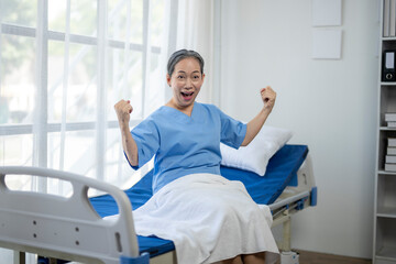 A woman in a hospital bed is smiling and raising her arms in the air