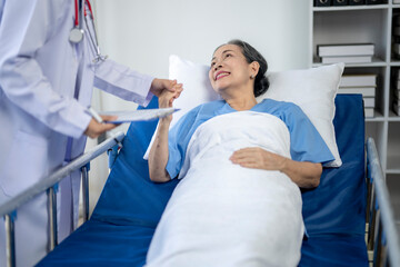 A woman in a hospital bed is smiling as a doctor hands her a clipboard