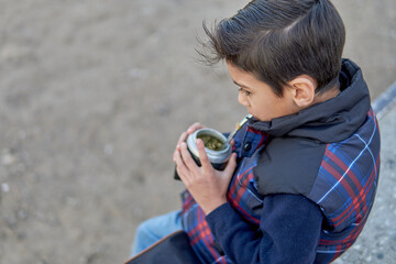 portrait of latin argentinian boy sitting outside drinking mate, close-up shot. Horizontal and copy...