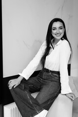 Happy smiled woman in formal denim style with white shirt sitting on chair.