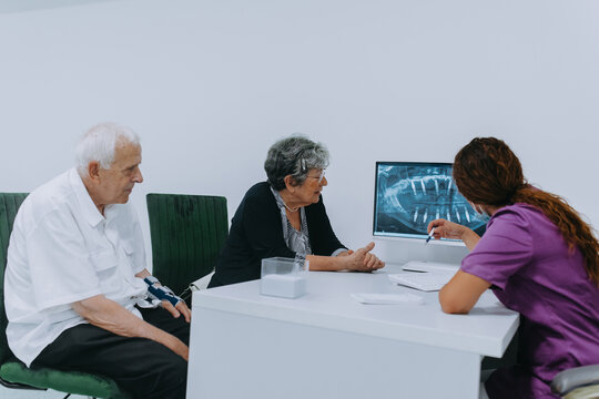 An elderly couple engages in a thoughtful discussion with their dentist about modern denture options in a contemporary dental office setting