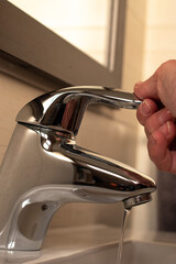 Close-up of a tap in a bathroom and a hand closing the tap. .General drought concept.