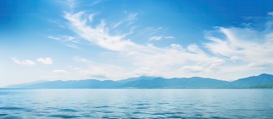 A serene summer seascape with clear water and beautiful blue sky adorned with white clouds Mountain silhouettes appear on the hazy horizon enhancing the tranquility and serenity of the ocean The imag