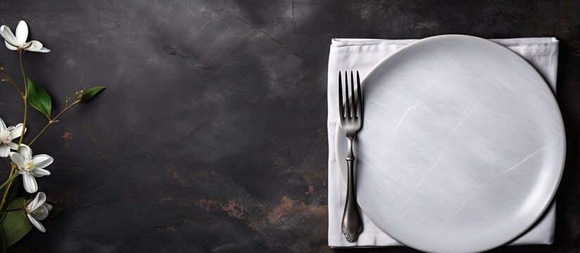 A top view of a white craft plate cutlery and napkin arranged on a dark stone table The table setting provides a background for a menu with a layout designed to accommodate text and a recipe backgrou