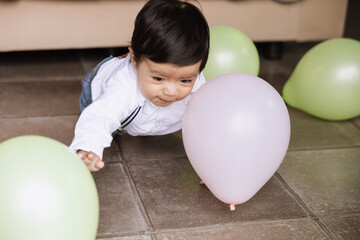 Joyful baby boy crawling among colorful balloons.