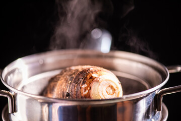 Steamed taro tuber in boiling pot steams up as a chef opens the lid of a pot.
