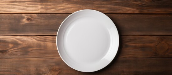 Top view of a white plate mockup placed on a dark wooden table background providing ample copy space for images