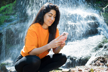 Fit Woman Looking her phone in the spring mountain on a waterfall background 