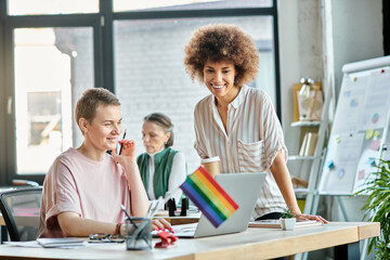 Attractive diverse businesswomen working together on project in office, pride flag.