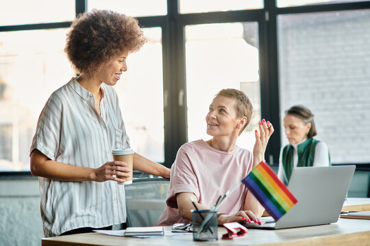 Cheerful diverse businesswomen working together on project in office, pride flag. - Powered by Adobe