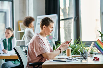 Short haired woman engrossed in work, with phone, with her diverse colleagues on backdrop.