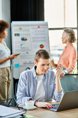 Short haired businesswoman engrossed in work on a laptop computer, with her diverse colleagues on backdrop.