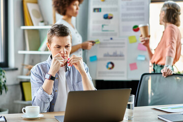 A businesswoman engrossed in work on a laptop computer, with her diverse colleagues on backdrop.